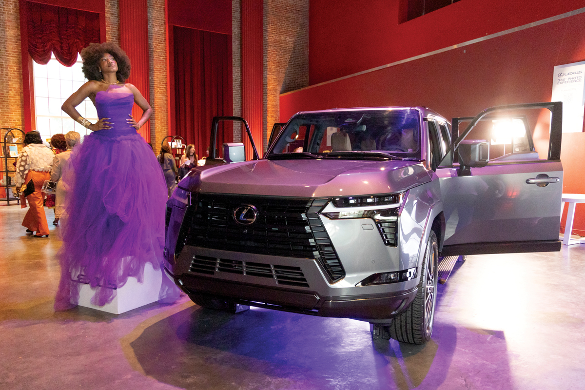 A model dressed by Menia Paige  Couture poses near a Lexus GX.