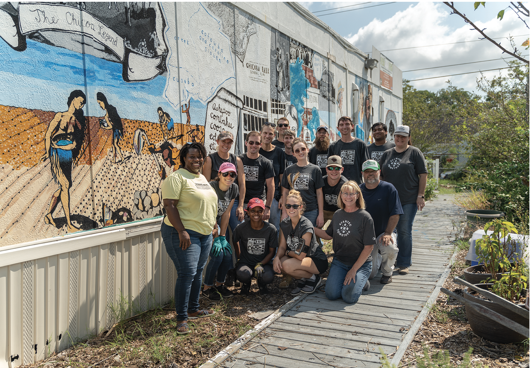 All Hands on Deck: The farm’s core team gets lots of help from volunteers, such as these employees from Stantec, pictured with Jenkins next to the farm store. The mural, which special projects manager Anik Hall researched, organized, and painted, depicts 500 years of the Chicora-Cherokee neighborhood’s history.