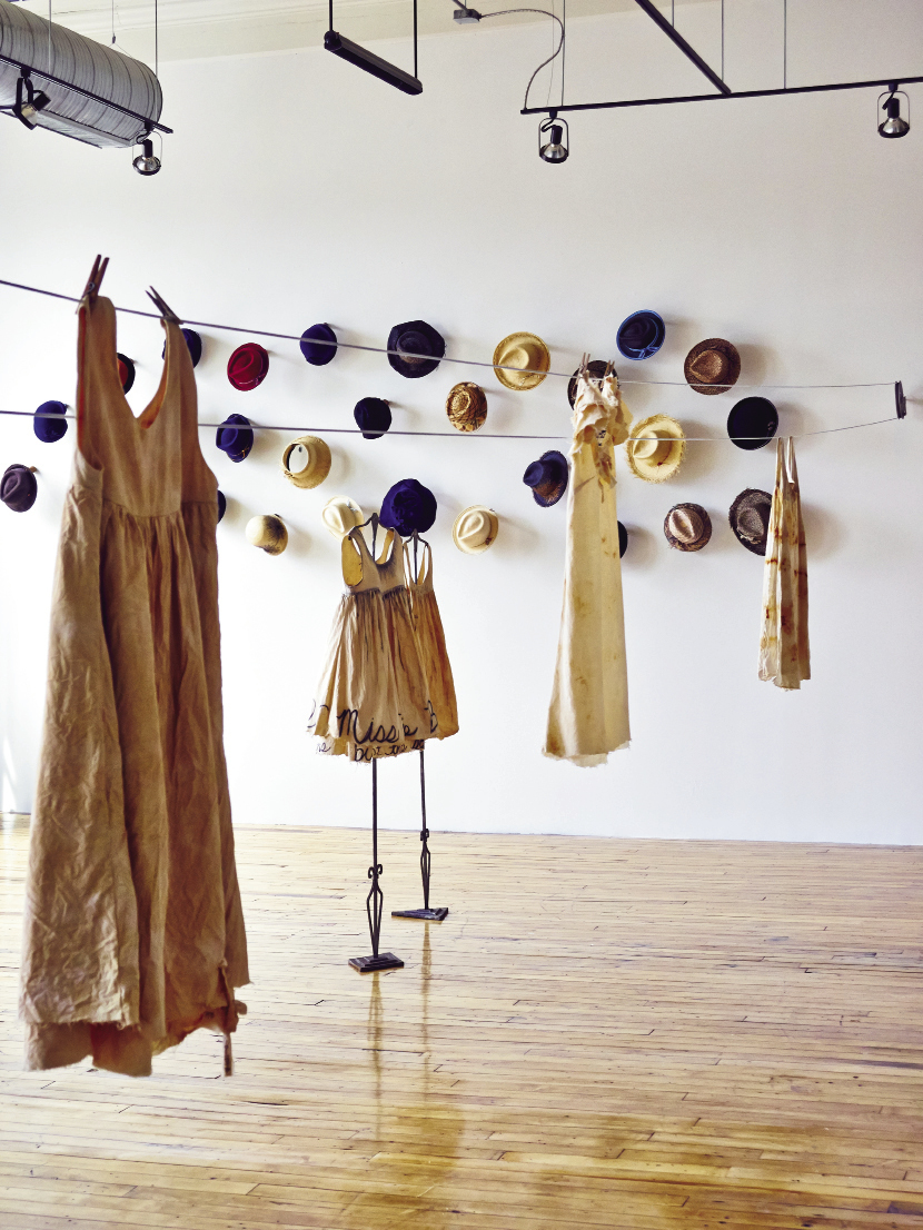 At the 701 Center for Contemporary Art, the new Madame Magar collection of muslin and canvas frocks hangs on pulleys and  hooks. As part of the exhibit, Charleston-based designer Leigh Magar has created a temporary studio workshop within the gallery space so  visitors can see her sewing, dyeing, and adding penciled lettering to the dresses.