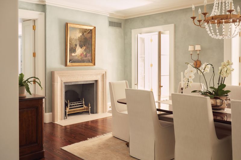 The aesthetic  continues into the dining room, where a matching limestone fireplace provides a stunning centerpiece against the restored plaster walls. Hand-chiseled by craftsman Simeon Warren, the limestone surround holds a reproduction brass-and-iron coal box crafted in England.