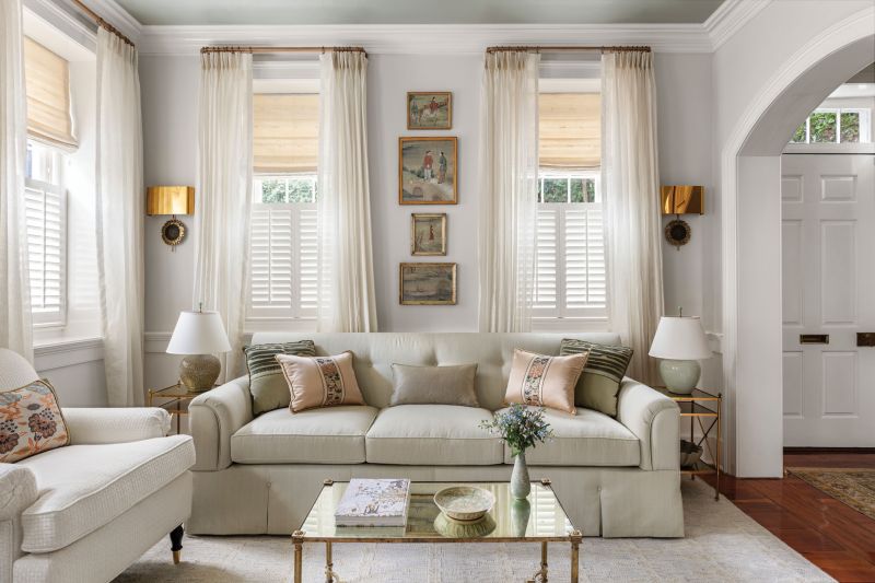 Soothing Sanctuary: The drawing room’s glossy, lacquered ceiling (Benjamin Moore “Misted Green”), soft color palette, and luxurious fabrics create a calm oasis for Claudia. “I love this space. It’s so peaceful to me.” The custom sofa, wrapped in Halsey &amp; Spruce raw silk, is flanked by luminous Sabina Fay Braxton fabric drapes. The antique Swedish secretary cabinet from The Painted Room harkens back to the home’s original era.