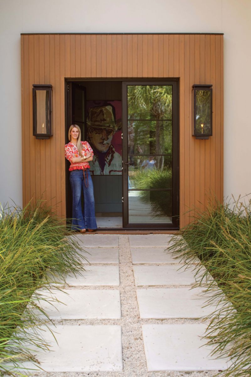 Claire stands in the home’s custom steel front door with Charleston-based artist Nathan McClements’ cowboy art behind her.