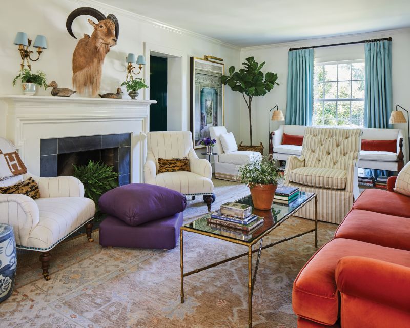 In the living room, neutral walls, rugs, and upholstery provide a cozy base for pops of persimmon (via the velvet sofa) and dusty blue (à la custom drapes and vintage sconces).