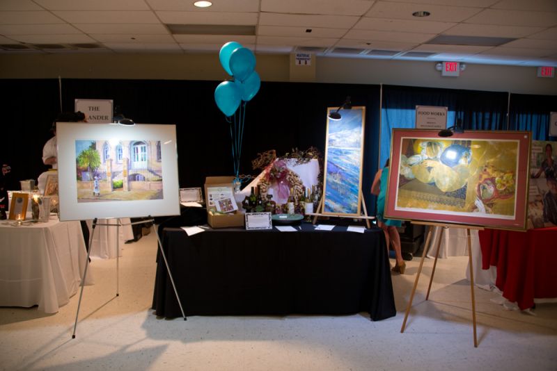 A table of silent auction items with wines, paintings, and a decorative cork wreath