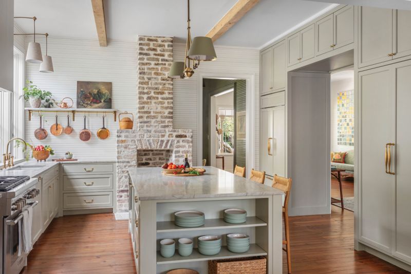 The fireplace backs into the kitchen, where the exposed brick chimney provides warmth and a unique architectural element. Cabinets painted in Farrow &amp; Ball “French Gray” complement the “Wimborne White“ walls.