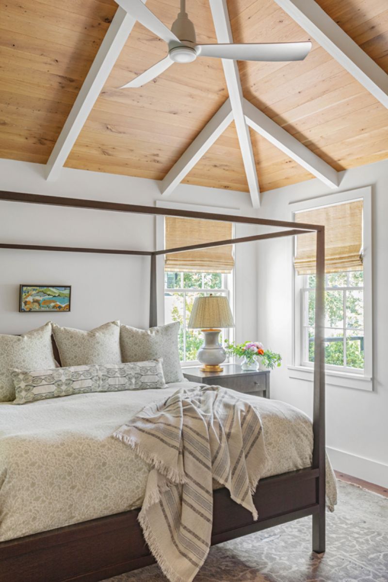 Vaulted ceilings are repeated in the primary bedroom suite, where white pine paneling and a four poster bed from Crate &amp; Barrel complete a simple but sophisticated space.