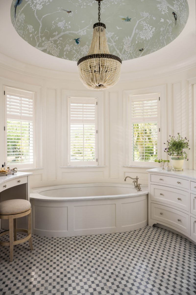 Curves continue in the primary bathroom where a striking Currey &amp; Company chandelier with glass beads hangs from a domed ceiling, painted by local artisan Angela Cabán. A mosaic tile floor of Carrara and Grigio Carnico marble grounds the elegant space.