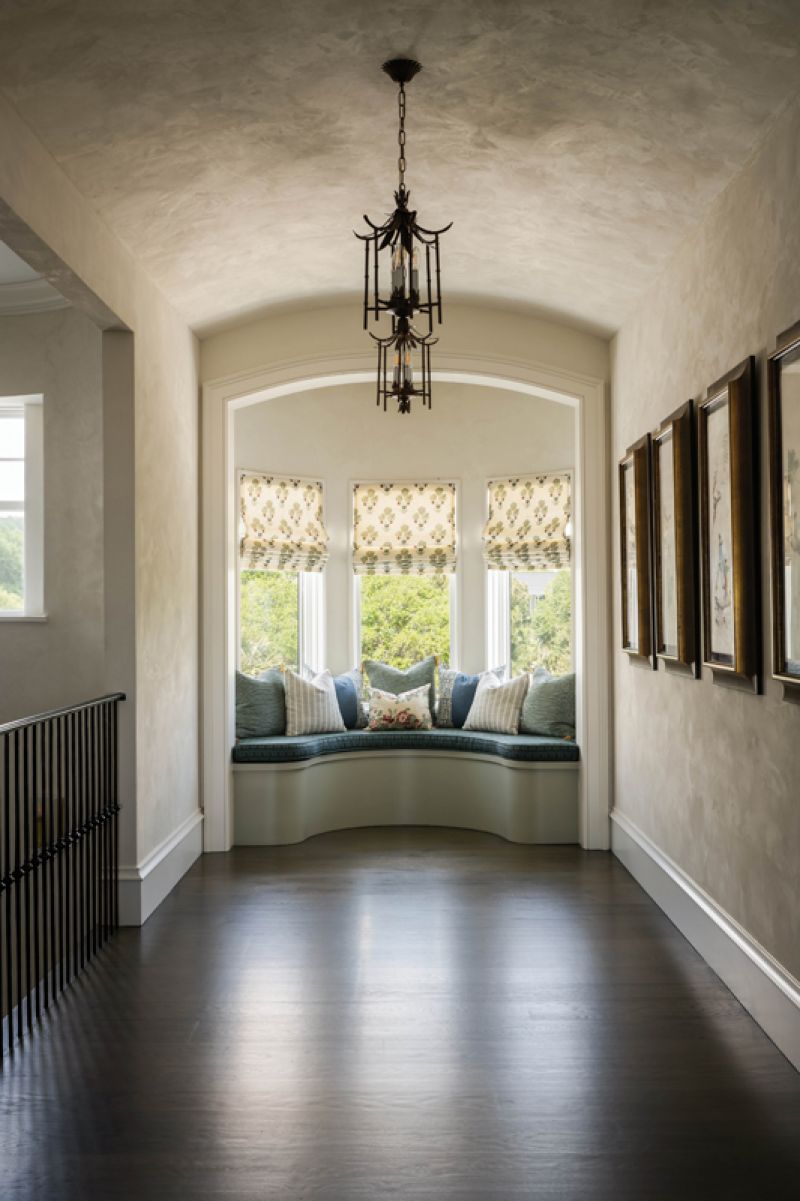 A curved window seat at the end of the gallery hall is upholstered with a Cowtan &amp; Tout fabric with pillows in textiles by Katie Leede &amp; Company, Rose Tarlow, and McLaurin &amp; Piercy.