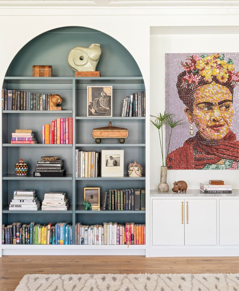 Top Shelf: Adding built-in bookshelves to the living room brought order to the room while providing a pop of color courtesy of Farrow &amp; Ball’s “Inchyra Blue.” The custom design also beautifully showcases local artist Molly B. Right’s bottle-cap homage to Frida Kahlo. A brass and wicker side table from Hollywood at Home and vintage shearling chair from 1stdibs add texture and dimension.