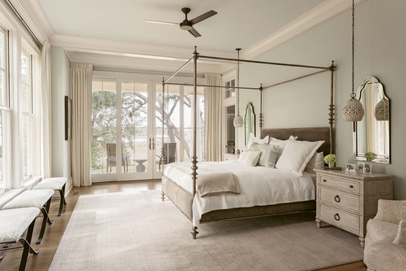 An upholstered four-poster bed from Southeastern Galleries welcomes views of the creek and the garden into the master bedroom. Pendant lights from Currey and Company replace traditional bedside table lamps, and large chests help reduce clutter in this calming space.