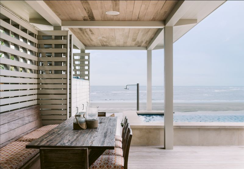 On the elevated courtyard, a slatted wall serves as a privacy screen while allowing breezes to flow through. “We eat out there as much as possible,” says Suzanne of the outdoor dining area with a large reclaimed wood table crafted by Landrum Tables. “We can enjoy a glass of wine while the kids are swimming.”